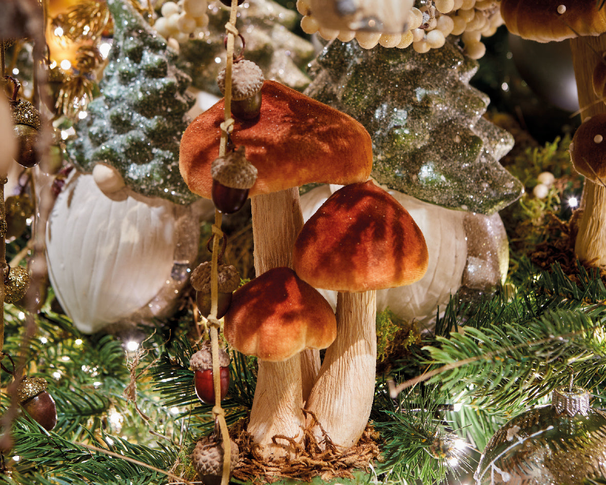 Funghi decorativi in velluto rosso appesi su un albero di Natale insieme a ghiande e altri addobbi tra i rami | DeMatteis.it