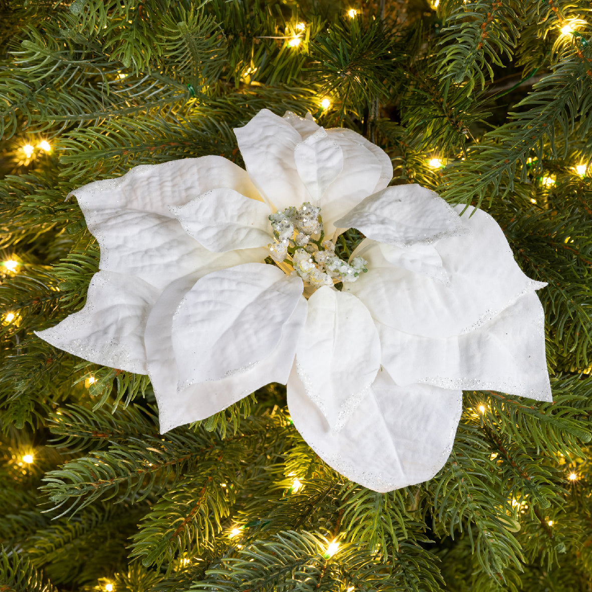 Stella natalizia bianca con glitter argentati posizionata tra i rami di un albero di Natale illuminato da lucine calde | DeMatteis.it