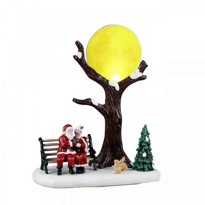 North Pole Romance Lemax con Babbo Natale e Signora Natale seduti su panchina sotto albero con luna dorata e conigli bianchi per Villaggio Natale Lemax | Dematteis.it