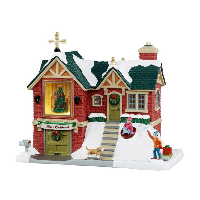 The Little Brick House Lemax del Villaggio Natale Lemax con facciata in mattoni rossi, tetto innevato, decorazioni natalizie e scene animate di bambini che giocano | Dematteis.it