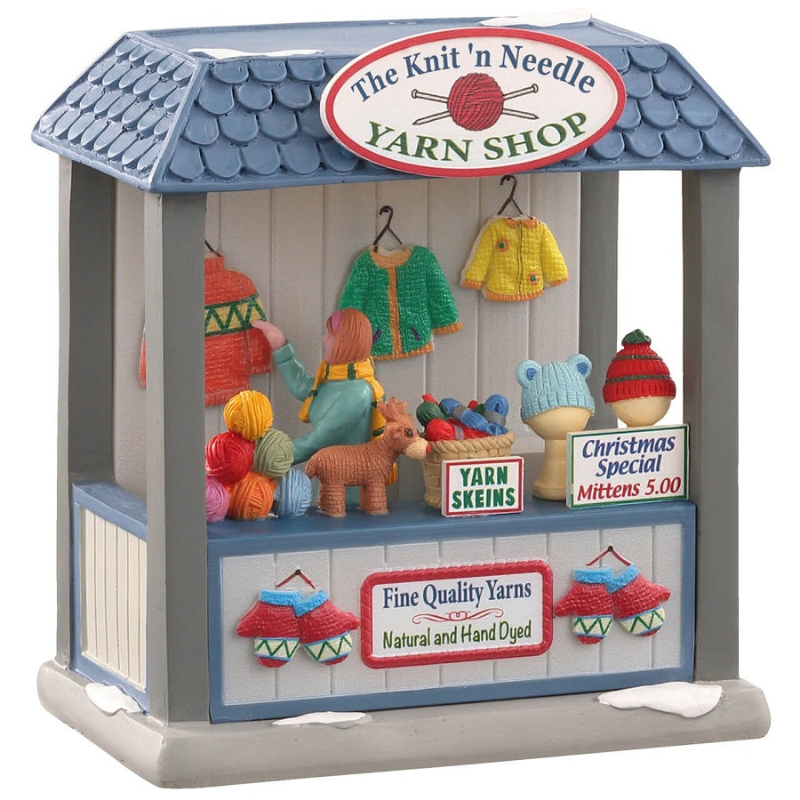 Bancarella dei filati Lemax The Knit'N Needle Yarn Shop con tetto blu, gomitoli colorati e capi invernali della collezione Caddington Village. | Dematteis.it