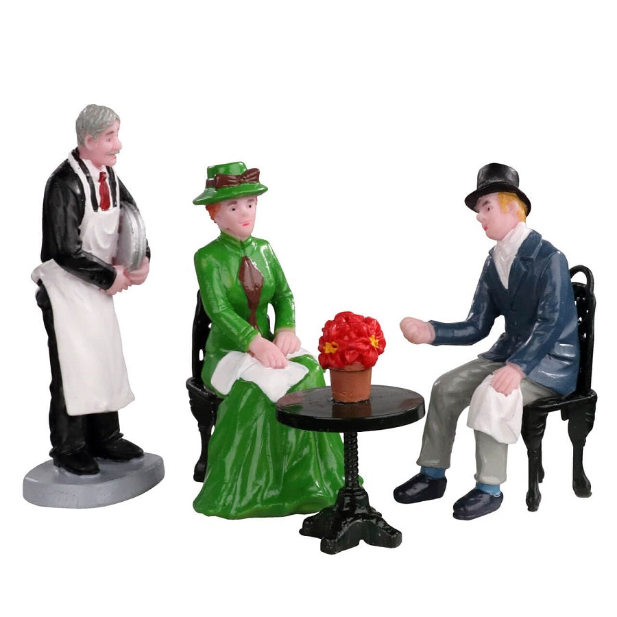 Statuina Lemax 'Café Society' che raffigura un cameriere che serve una coppia seduta a un tavolo. La scena presenta costumi d'epoca, con la donna in abito verde e l'uomo con cappello a cilindro. Perfetto per villaggi Lemax vintage - Dematteis.it